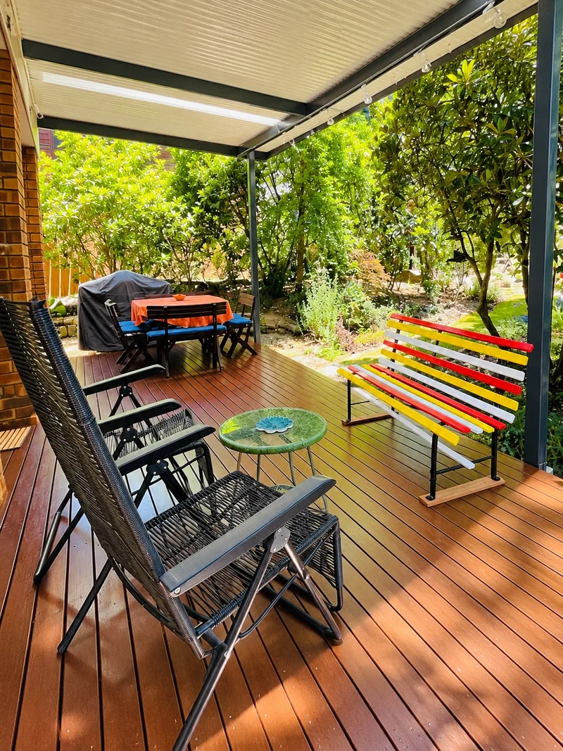 Covered deck overlooking the cottage garden, with colourful bench and outdoor seating